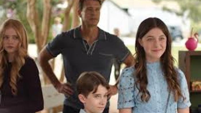 A dad with hands on his hips, and three kids, two girls and a boy, looking off camera. Their ages range from 10-mid-teen