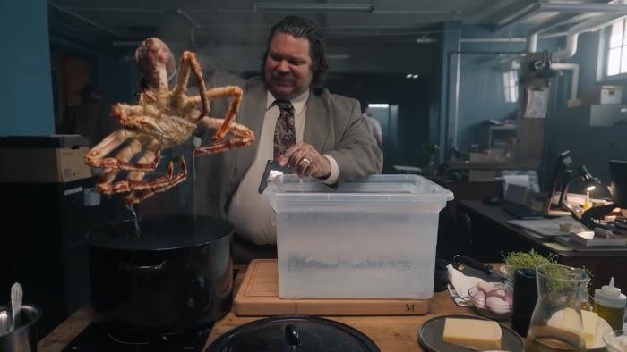 Just a Dash TV show screenshot 3: Matheson pulls a giant king crab out of a pot. He wears a gray suit jacket, white shirt, badge, and patterned tie.