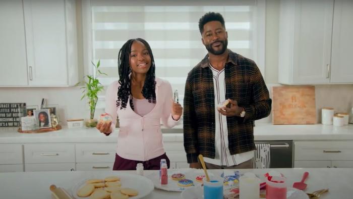Kids Pick The President screenshot: Mia Burleson and her dad Noah Burleson look at the camera in their white kitchen, backing election-themed cookies.