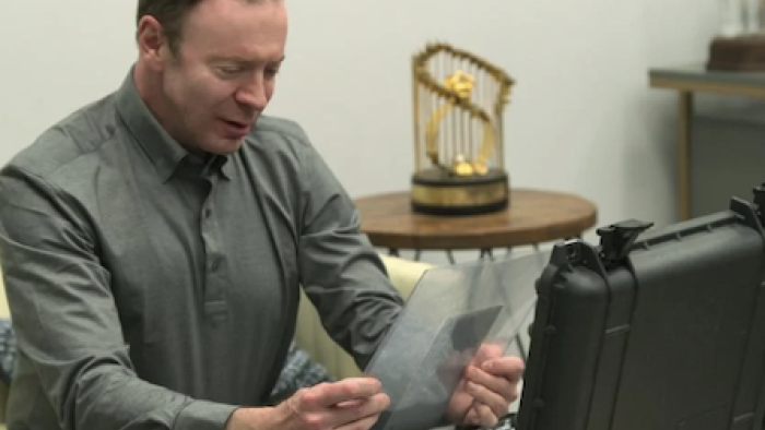 King of Collectibles: The Goldin Touch screenshot 1: Ken Goldin sits left on sofa holding valuable piece of paper in clear envelope with both hands. 