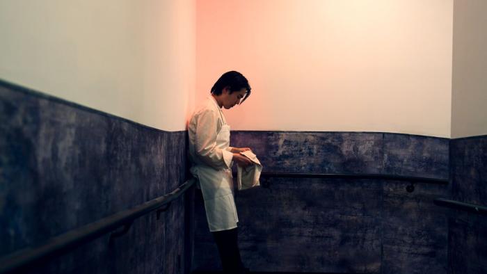 Knife Edge: Chasing Michelin Stars TV show screenshot: An Asian chef stars at the floor staring down at the floor standing in an empty room.