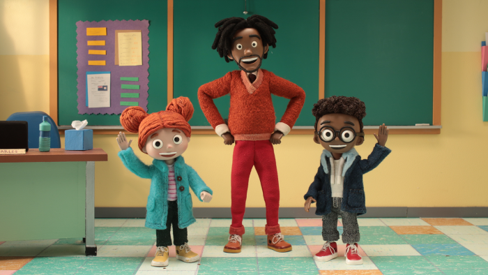 Know Your Rights University TV: Lisa, Mr. C and Aaron in the classroom, wave at the camera with hands raised.