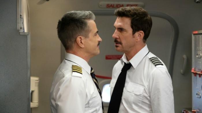 LA to Vegas TV Show: Two pilots stand together in a plane galley; they are standing close together and appear to be arguing. 