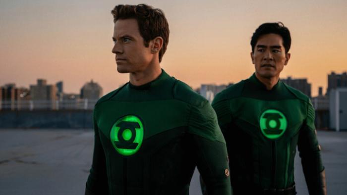 Lanterns: Two Lanterns in Green Lantern costumes with glowing green insignias on the chest are seen against a cityscape at sunset