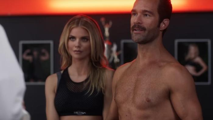 Let's Get Physical Series: A man and a woman stand together; she is wearing an aerobics leotard, he is shirtless; both are talking to someone else off-camera. 
