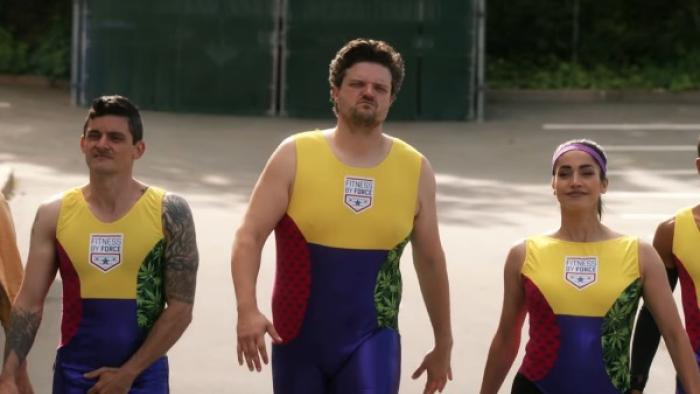 Let's Get Physical Series: Two men and a woman are walking confidently into camera; each is wearing a neon-yellow and blue aerobics unitard. 