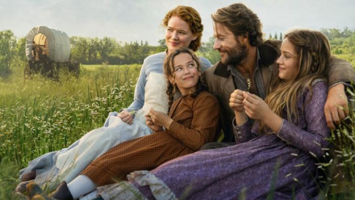 Little House on the Prairie TV show: Mary, Laura, Charles, and Caroline sit close together on a green stretch of prairie, their wagon behind them