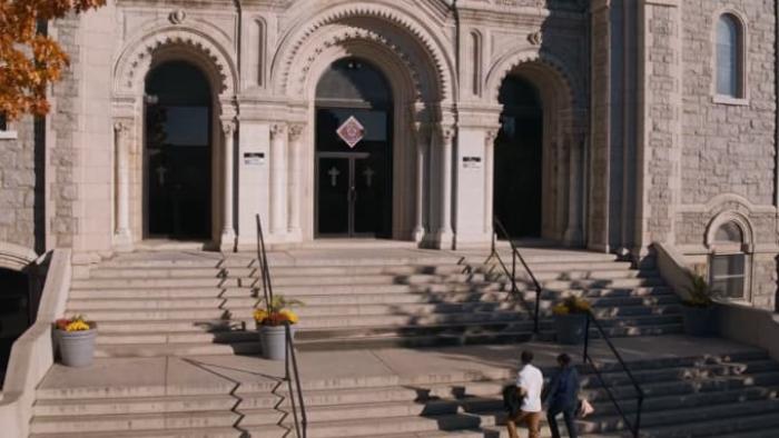 Living Undocumented Series: Two men walk up a set of stone steps into the civic building looming over them. 