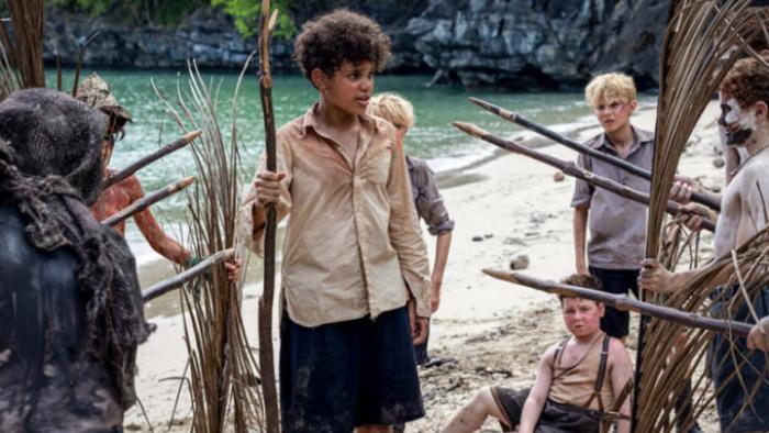 Lord of the Flies TV show screenshot 2: Ralph stands helplessly between two lines of boys with sharpened stakes, under attack