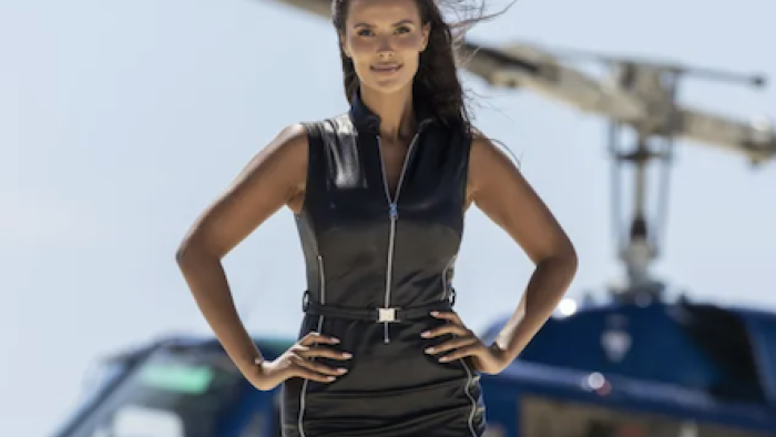 Love Island Games TV show screenshot 1: Maya Jama in black leather on beach in front of helicopter.