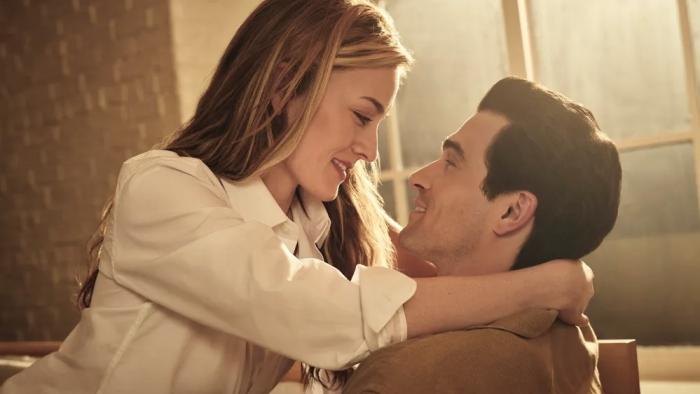 Love Story TV show screenshot 2: Sarah Pidgeon and Paul Anthony Kelly lay on a chair. Pidgeon wears a white top, while Kelly wears a brown shirt.