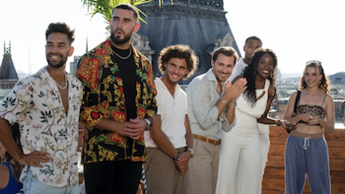 Still from Love Trip: Paris: Suitors of different genders and races stand on the roof deck of their apartment building