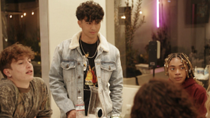 Love ALLways screenshot 2: Male contestant wears jean jacket and stands next to table where others are sitting. 