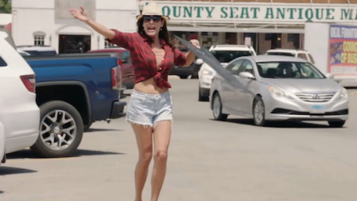 Luanne & Sonja: Welcome to Crappie Lake TV show screenshot 2: LuAnn runs through parking lot in white short and purple low cut blouse, hat, sunglasses. 