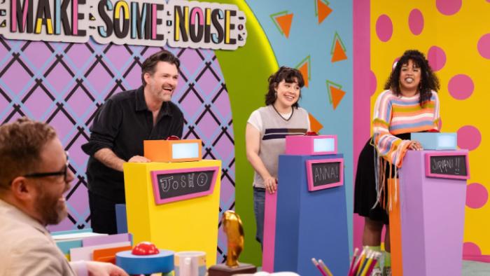 Make Some Noise: Josh Ruben, Anna Garcia, and Jiavani Linayao stand behind colorful contestant podiums on the Make Some Noise set