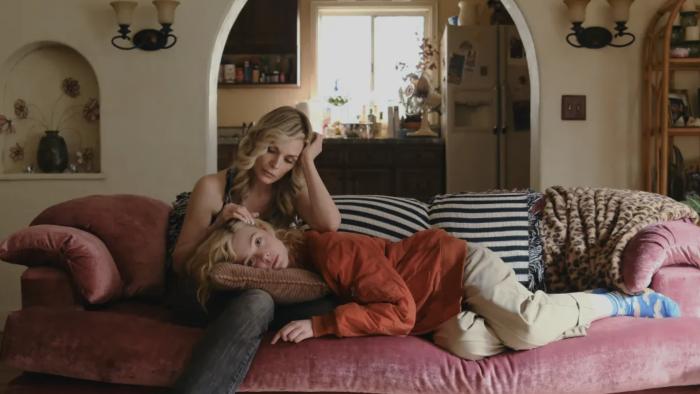 Michelle Pfeiffer sits on a velvet couch, with Elle Fanning laying her head on her lap.