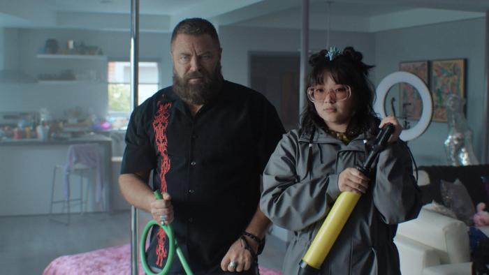 Nick Offerman and Thaddea Graham. Offerman wears a black shirt with red graphics. Graham wears a grey coat and pink glasses.