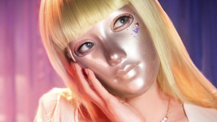 Mask Girl TV show screenshot 1: Woman in gold mask and blonde wig leans her face in her hand. 