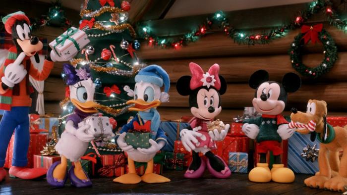 Mickey's Christmas Tales TV show screenshot: Mickey and his friend stand side by side in a house decorated for Christmas, putting presents around a Christmas tree.