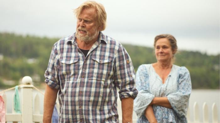 Midsummer Night: A middle aged man and woman walk but not together. The man in a plaid shirt walks ahead of the woman.