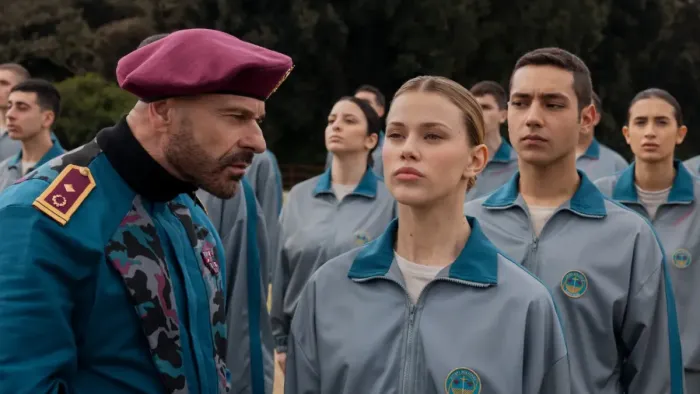 Minerva Academy TV show screenshot 3: Esposito in military gear and a beret looks cross at Camila, in uniform, surrounded by students outdoors.