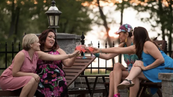 Mohawk Girls TV Show: Zoe and Caitlin sit across from Anna and Bailey on lawn chairs, toasting pink cocktails.