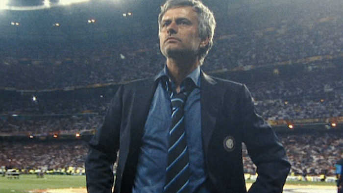 Mourinho TV show screenshot 1: José Mourinho in a suit stands confidently on a soccer field, stadium lights shining behind.