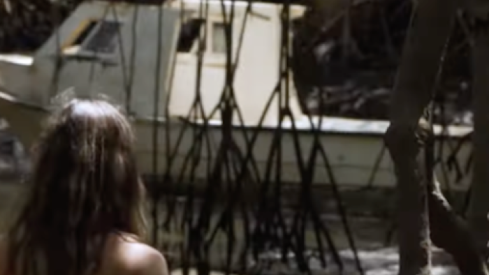 Naked and Afraid Castaways screenshot 3: A cast member looks at a white boat through branches.