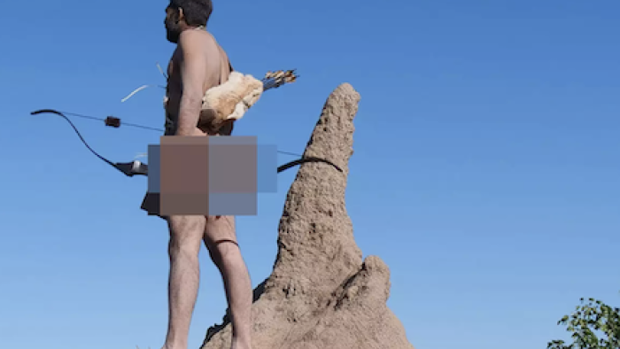 Naked and Afraid: Solo: Fernando Calderon stands with bow and arrows next to pointed rock and looks out left. 