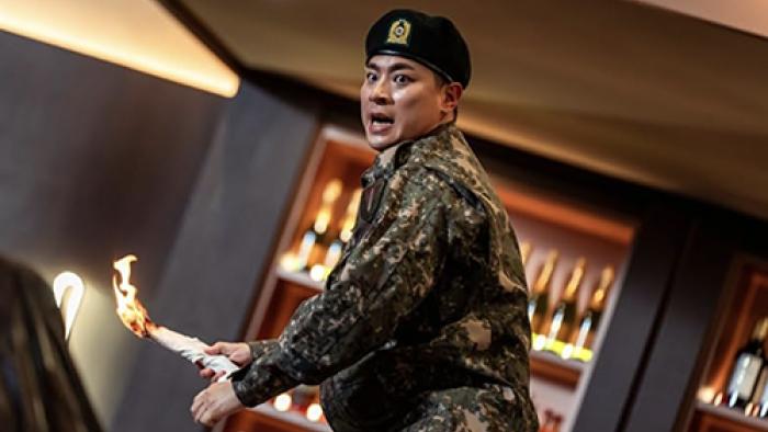 Newtopia TV show screenshot 2: Jae-yoon wears his military uniform while standing in front of a bar, about to throw a rolled-up napkin that's on fire