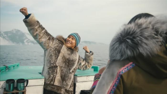 North Of North TV show screenshot 1: Siaja has her back to the camera, photographing Ting who poses with one arm up in a boat. 