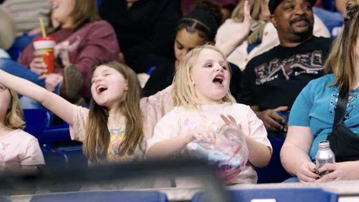 Not Her First Rodeo TV show screenshot 3: A rodeo crowd, fronted by two excited little girls, cheers on the bull rider