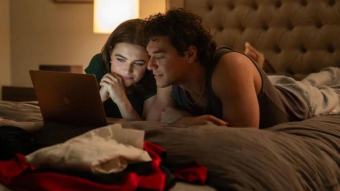 Off Campus TV show screenshot 3: Hannah and Garrett lie on their stomachs together on a bed, looking at something on a laptop computer