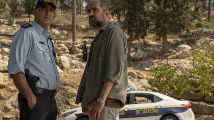 Our Boys Television Scene 1: Investigators meet up to share knowledge in front of a police car parked by a large rocky hill. 
