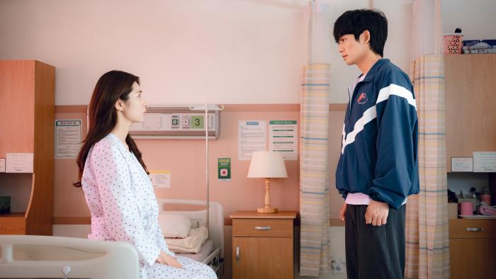 Ha-young and Jung Hae-in. Ha-young sits on a hospital bed, wearing patient attire. Jung wears a blue jacket and sweatpants.