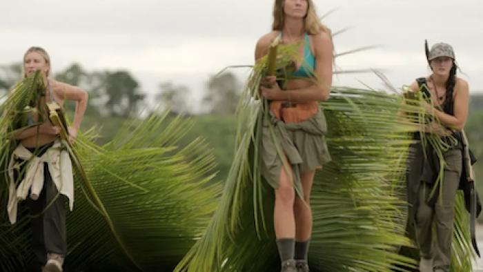 Outlast: The Jungle TV show screenshot 3: Three women carry large palm fronds on a cloudy day.
