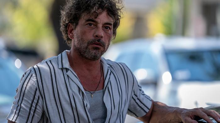 Actor Skeet Ulrich as Colin is pictured wearing a short-sleeved white shirt. He has bruises on his face