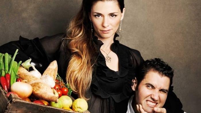 The Pasta Queen TV show screenshot 1: A woman hold veggies in one hand, and has a man in a loose headlock in the other.