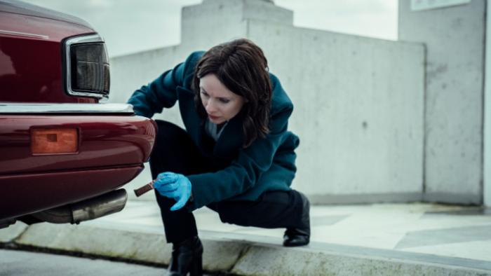 Patience TV show screenshot 2: Detective Bea looks at the rear bumper of a car with a flashlight