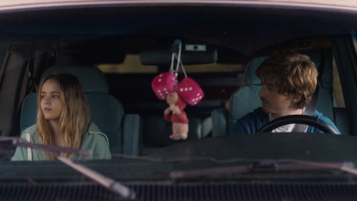 Penelope and Sam sit in the front seat of Sam's van, a set of pink fuzzy dice hang from the rearview mirror