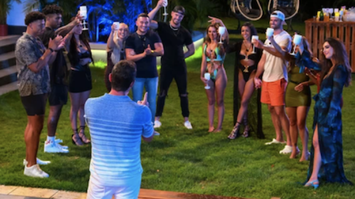 Perfect Match TV show: Nick Lachey stands with back to camera in a toast with contestants. 