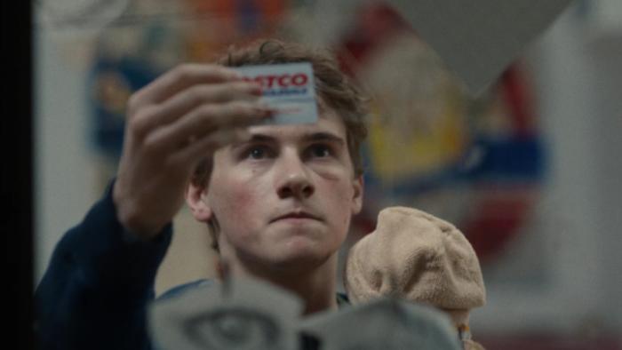 Phony TV show screenshot 2: Sonny holds up a Costco card, trying to compare its picture with his mother's face in real life