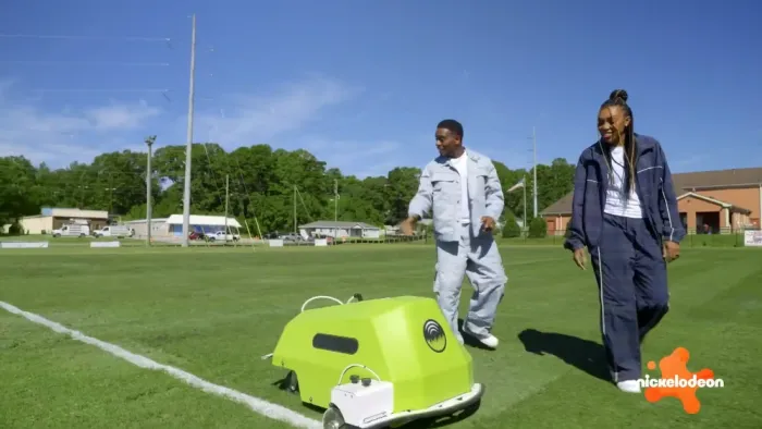 Play It Forward TV show screenshot 3: Kel Mitchel and Renee Montgomery watch a field liner robot draw white lines on a soccer field.
