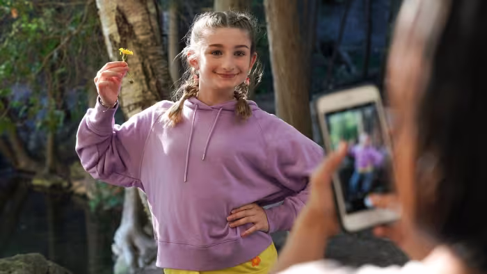 Popularity Papers TV show screenshot 2: Lydia shows off a single daisy as she poses for a photo in her hiking clothes. 