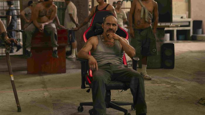 Prison Cell 211 TV show screenshot 2: Noé Hernández sits in a black and red office gaming chair, surround by inmates. 