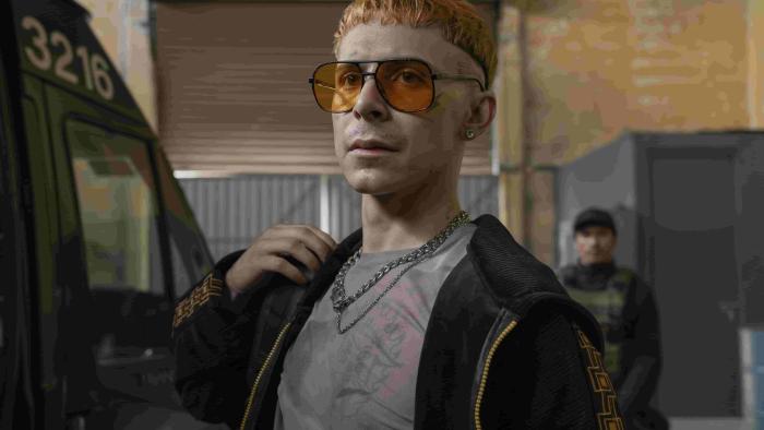 Prison Cell 211 TV show screenshot 3: Alejandro Puente wears a grey T-shirt, black velvet zip-up hoodie, and sunglasses with orange lenses. 