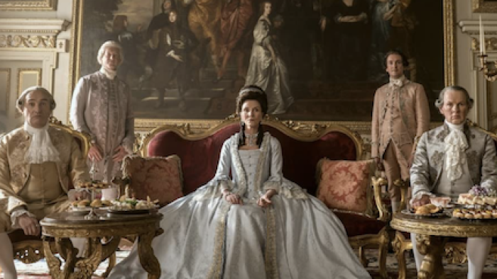 Queen Charlotte Screenshot 3: Princess Augusta sits in a blue Regency-style dress with advisors and government officials. 