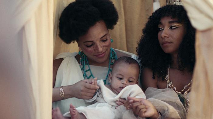 Queen Cleopatra TV show: Cleopatra rides in a carriage with one of her advisers and her infant son; all are dressed in white. 