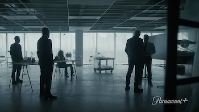 Rabbit Hole TV show: Four men stand and one woman sits at a desk in a mostly empty room with low lighting