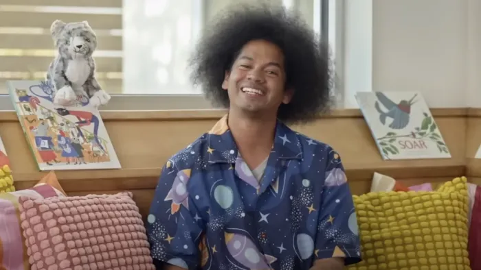Reading Rainbow TV show screenshot 1: Host Mychal the Librarian smiles broadly at the camera in a cozy space surrounded by books.